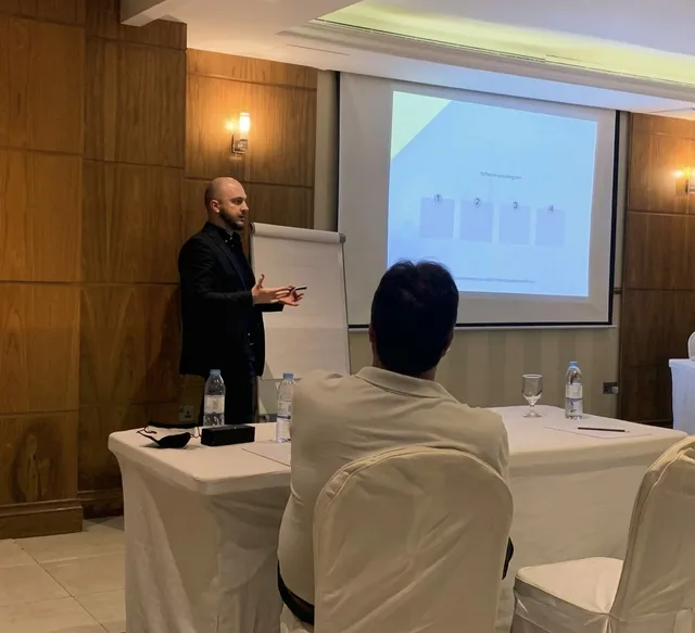 Mikail presenting beside a projection screen and flip chart.